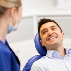 A middle-aged man lying back in a dentist’s chair and smiling at his dentist as she explains the process for receiving a dental crown
