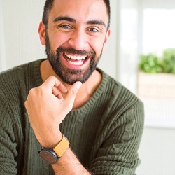 A gentleman wearing a watch and green sweater smiling after receiving his dental bridge