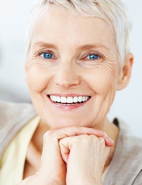 An older woman with short, blonde hair, clasping her hands together and smiling after receiving her dental crowns in Myrtle Beach