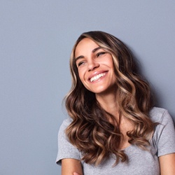 A young woman with her arms crossed smiling and looking off to the side, happy about her results from gum recontouring