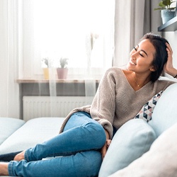 A young woman seated on a couch and smiling, enjoying her new and improved appearance