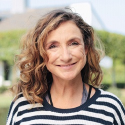 An older woman wearing a striped sweater and smiling after receiving her new dental implants