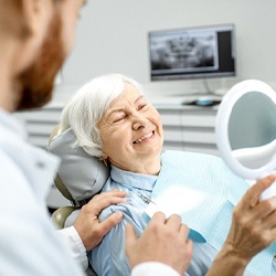 A dentist talks to an older woman while she looks at her smile in the mirror at the dentist’s office