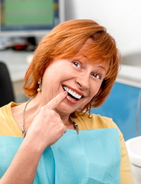 A middle-aged woman with red hair pointing to her new teeth after learning how dental implants work in Myrtle Beach