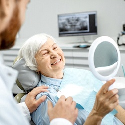 A dentist talks to an older woman while she looks at her smile in the mirror at the dentist’s office
