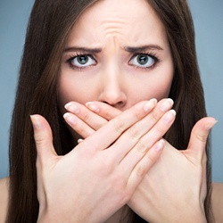 A woman holding her hands over her mouth because of her bad breath
