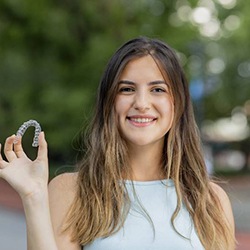 Smiling young woman holding aligners from her Myrtle Beach cosmetic dentist 