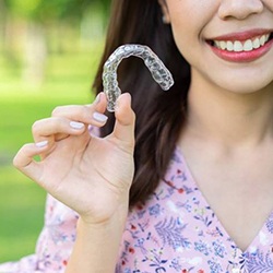 Closeup of smiling woman holding Invisalign outside