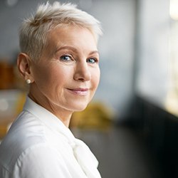 An older woman wearing a white blouse and smiling while seated indoors