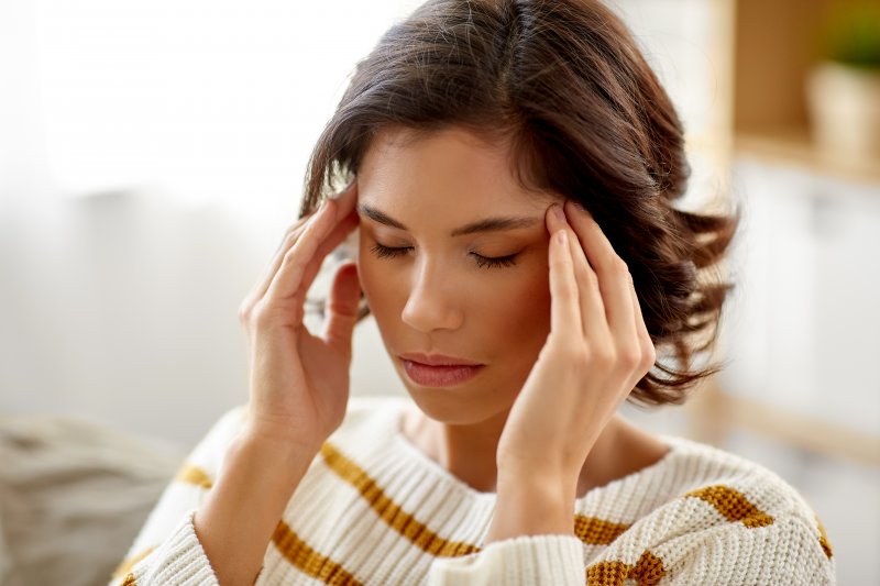 a young woman wearing a sweater and rubbing her temples due to stress