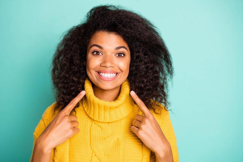 a young woman wearing a yellow sweater and pointing to her healthy smile