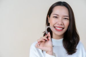 Woman smiling and holding her Invisalign tray.